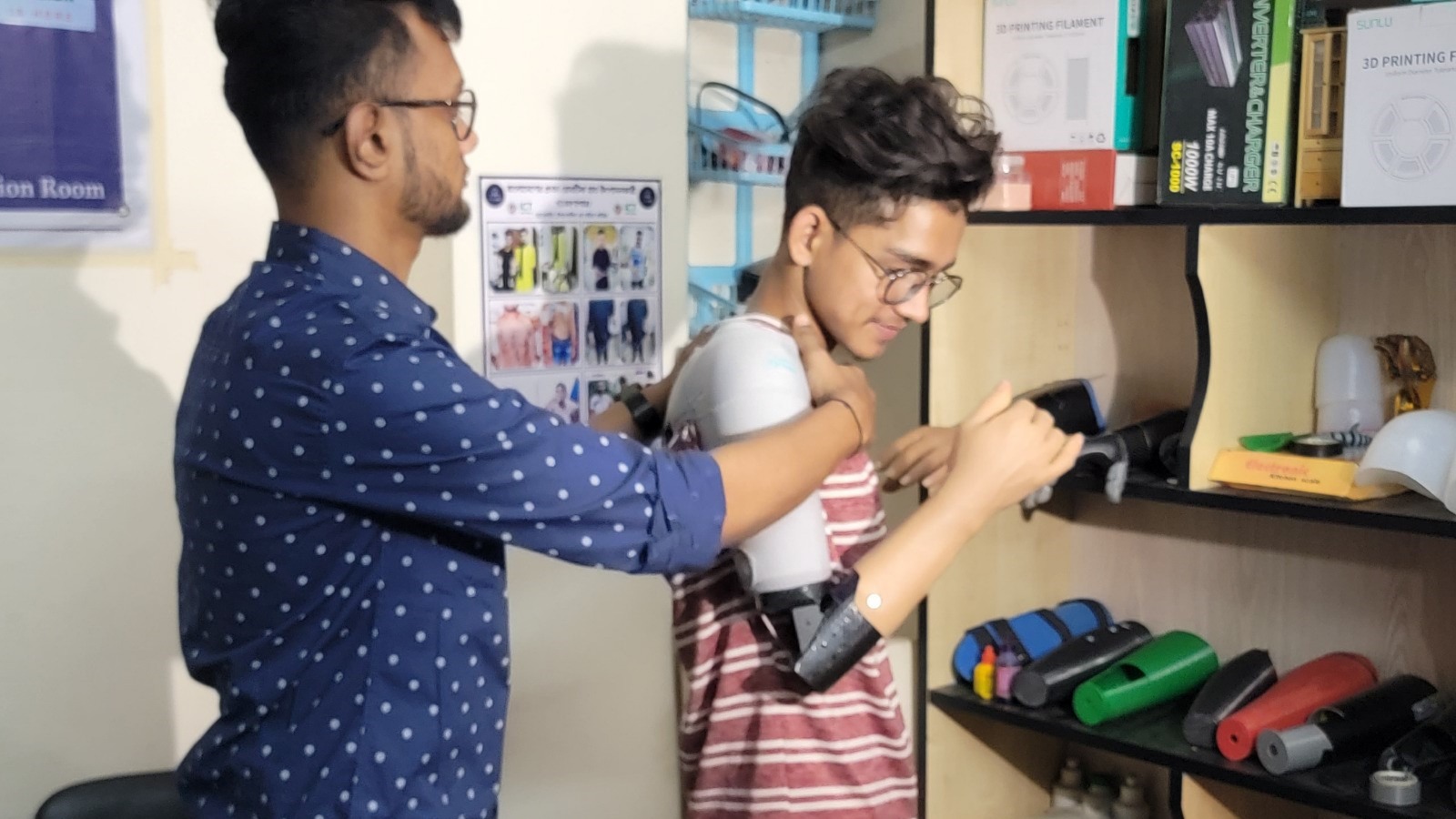 রোবোলাইফ টেকনোলজির প্রতিষ্ঠাতা জয় বড়ুয়া আতিকুল ইসলামকে কৃত্রিম ডান হাত প্রতিস্থাপন করে দিচ্ছেন।